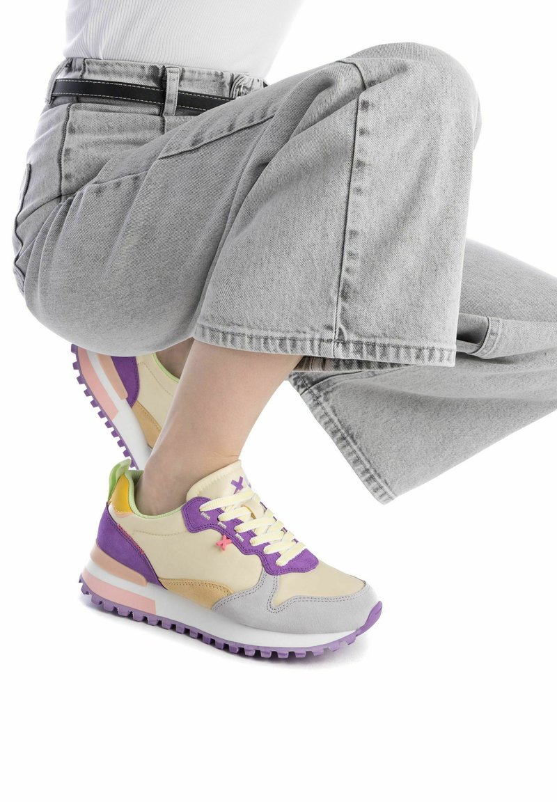 Sneaker multicolore con una tomaia crema, accenti viola e gialli, un puntale testurizzato e una suola imbottita con una striscia rosa.
