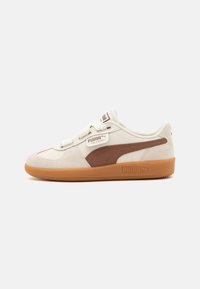PUMA sneakers ar krēmkrāsas ādas virsu, brūna zamša akcentu un gumijas zoli; apaļa purngala forma, plakani šņorējumi un zīmols sānos.
