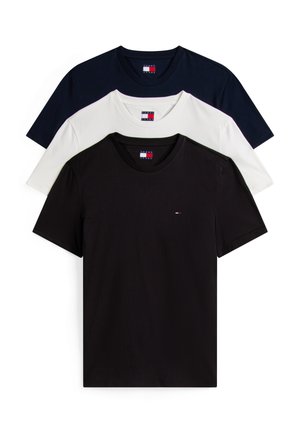 Fiatal férfi áll zsebre tett kézzel, mentazöld sapkában, sötétkék pólóban kockás ing fölött, világoskék farmernadrágban és fehér sportcipőben.