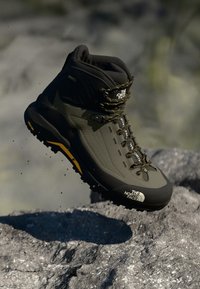 Buty trekkingowe w czarno-oliwkowym wzorze, z teksturowanym syntetycznym cholewką, grubą gumową podeszwą i żółtymi akcentami.