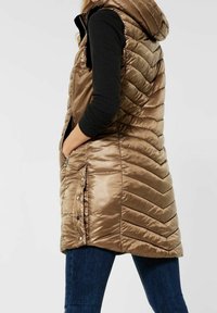 Bronsfärgad pufferväst i ankellängd med huva, prydd med chevron-stickning, dragkedjefickor i sidorna och tryckknappsdetaljer. Mjuk, glänsande yta.