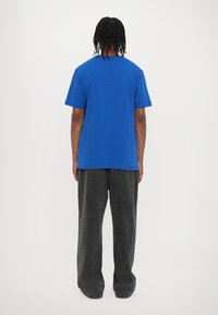 Blue cotton T-shirt with short sleeves, basic design. Paired with loose-fitting gray trousers, soft texture, and wide legs.