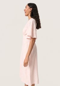 Rochie roz, până la genunchi, cu mâneci scurte evazate. Realizată dintr-un material cu perforații, cu modele florale decupate. Textură netedă și croială lejeră.