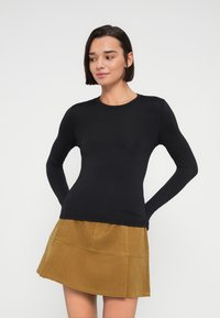 Μαύρο μακρυμάνικο τοπ από λείο, ελαστικό ύφασμα, με στρογγυλή λαιμόκοψη, συνδυασμένο με κίτρινη μίνι φούστα από κοτλέ ύφασμα.