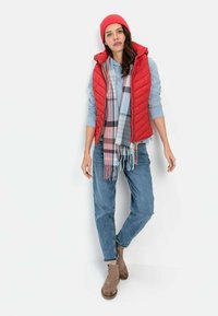 Rød quiltet vest, lyseblå langærmet skjorte, ternet tørklæde i blå og pink, blå jeans og brune ankelstøvler.