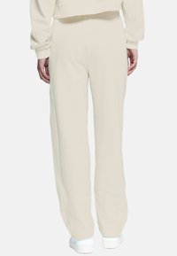 Pantaloni della tuta beige con una vestibilità rilassata, caratterizzati da una texture liscia e una vita elastica, abbinati a sneakers bianche.