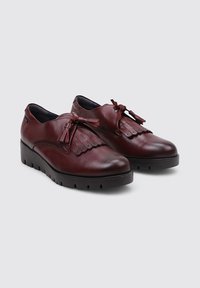 Zapatos de cuero burdeos con punta redonda, detalle de flecos y cordones decorativos; suela de goma negra gruesa con patrón acanalado.