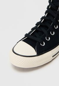 Μαύρο σουέντ αθλητικό παπούτσι με λευκή λαστιχένια μύτη, κρεμ λεπτομέρειες, μαύρα κορδόνια και μεταλλικά ρυγχοειδή τρύπες. Διαθέτει υφασμένο λαστιχένιο πέλμα.