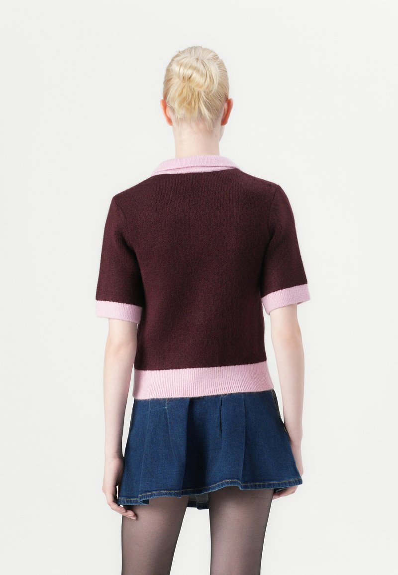 Korte mouwen maroon trui met een roze kraag en zoom, gemaakt van een textuurstof, gecombineerd met een denim rok en zwarte maillots.