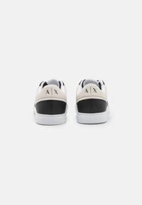 Sorte og beige lær-sneakers med en hvit såle, med logodetalj på hælen og et glatt design. Kontrastene i tekstur er tydelige.
