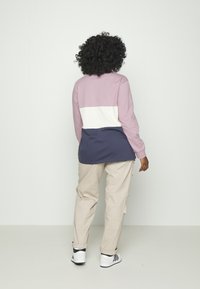 Farbblockiertes Sweatshirt in Pink, Weiß und Marineblau; lockere Passform mit langen Ärmeln; kombiniert mit beigen Cargo-Hosen und schwarz-weißen Sneakers.