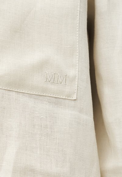 Κοντινό πλάνο σε κρεμ χρωματιστό λινό ύφασμα με ραμμένα αρχικά "MM" σε διπλωμένη γωνία.