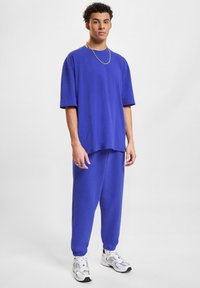 Veľký dvojdielny outfit z jasne modrej látky. Tričko s krátkym rukávom a okrúhlym výstrihom, vo voľnom strihu, kombinované s joggermi s elastickými šnúrkami.