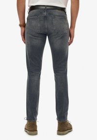 Jeans gris oscuro con un corte ajustado, que presentan bolsillos traseros y una sutil textura desgastada. Llevados con un cinturón negro y botas tipo chelsea marrones.