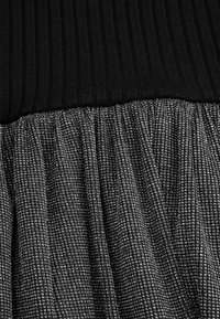 Czarny ribbowany top przechodzi w teksturowany czarny i srebrny plisowany materiał, wyróżniający się subtelnym wzorem siatki i miękkim wykończeniem.