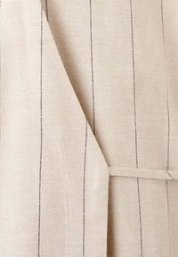 Tissu beige avec fines rayures verticales noires, comprenant une couture ajustée et une boucle de ceinture en tissu assorti sur le côté.