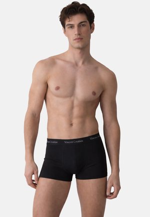 Shirtless male model wearing black Vincent Creation boxer briefs, standing against a plain light gray background.