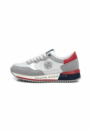 Zapatilla gris y blanca con materiales de ante y piel. Presenta una suela texturizada, acentos en rojo y azul marino, y un logo en el lateral.