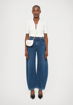 Jeans in denim blu a gamba larga abbinati a un top bianco aderente con scollo all'americana, abbelliti da una piccola borsa a tracolla color crema.