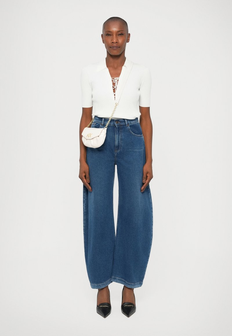 Laiad sinised denim püksid, mis on kokku sobitatud istuva valge pluusiga, millel on nööriga dekoltee, ja väikese kreemika ristseljakotiga.
