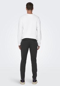 Chemise blanche à manches longues associée à un pantalon gris foncé. Le tissu semble doux avec une coupe décontractée. Les chaussures présentent une semelle et un design multicolores.
