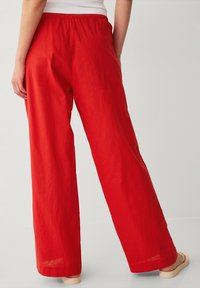Pantaloni larghi in lino rosso con vita elastica, texture liscia e vestibilità rilassata, mostrati da una vista posteriore.