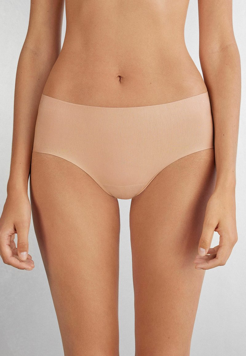 Naadloze huidkleurige hipster slipjes van glad, rekbaar materiaal met een lage tailleband, met een minimalistisch ontwerp en zonder zichtbare stiksels.