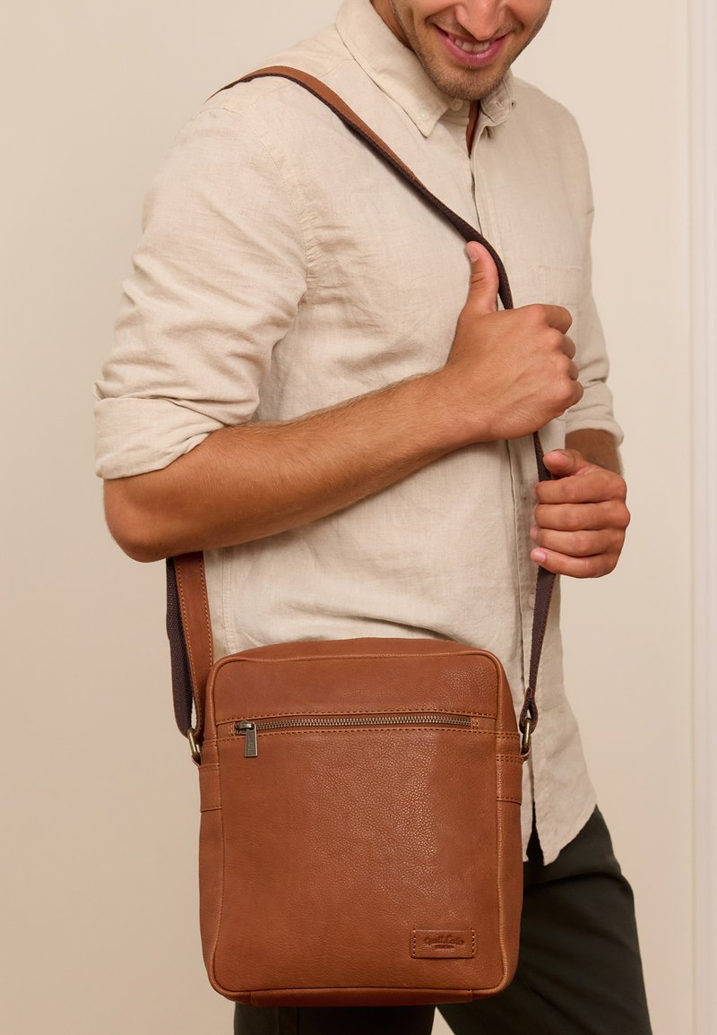 Brązowa skórzana torba na ramię z fakturowaną powierzchnią, zamek błyskawiczny i regulowany pasek, noszona na ciele, z przednią kieszenią.