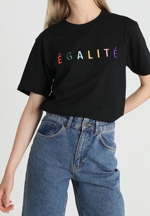 Černé bavlněné tričko s krátkým rukávem, na přední straně s vícebarevným vyšitým nápisem "ÉGALITÉ", spárované s modrými džíny.