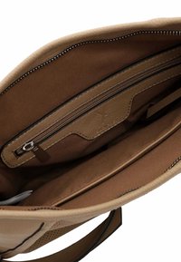 Interno di una borsa a tracolla in pelle color tan con una tasca con zip, foderata in tessuto marrone, e uno spazio aperto per l'organizzazione. Presenta una chiusura con zip superiore.