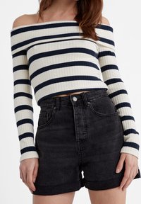Pull en crème et marine à épaules dénudées, texture côtelée ; short en denim noir taille haute avec fermeture à bouton et ourlet retroussé.
