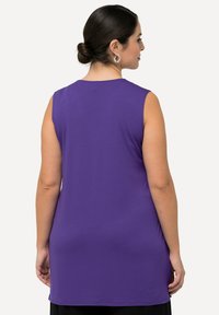 Top senza maniche viola realizzato in morbido tessuto, con scollatura rotonda e orlo leggermente più lungo sul retro per una vestibilità comoda.