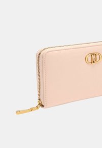 Portafoglio in pelle rosa blush con zip e hardware dorati. Presenta un dettaglio del logo circolare sul fronte. Texture liscia, design minimale.