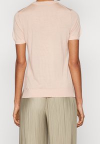 Světle růžový pletený top s krátkými puffovými rukávy a kulatým výstřihem, který se vyznačuje hladkou texturou a žebrovaným lemem. Zobrazeno ze zadní strany.