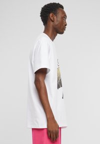 Hvid bomulds t-shirt med korte ærmer, der har et iøjnefaldende grafisk tryk foran. Pasformen er afslappet og komplementerer sidevinklen.