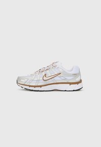 Bijele sportske tenisice sa srebrnim detaljima, izrađene od mrežastih i sintetičkih materijala, s dizajnom na vezanje i teksturiranim gumenim đonom. Nike logo sa strane.