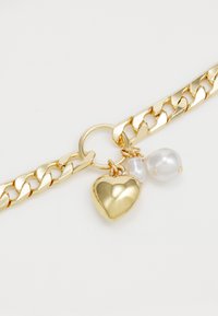 Gold chain bracelet featuring a shiny heart charm and two pearl accents, showcasing a sleek, polished finish and interlocking links.