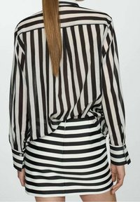 Chemise à manches longues rayée noire et blanche avec une coupe décontractée, associée à une minijupe rayée ajustée, mettant en valeur des motifs contrastés.