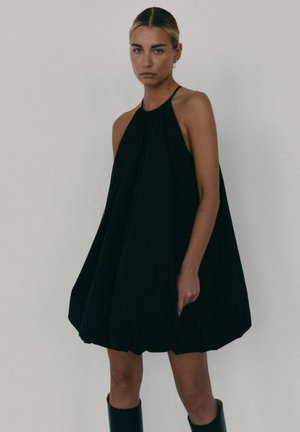 Czarna sukienka bez rękawów z dekoltem halter, posiadająca luźną, obszerną sylwetkę i marszczony dół. Gładki materiał bez wzorów ani dodatków.