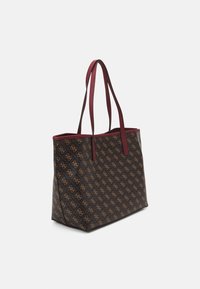 Brązowa torba na ramię z wzorem, z beżowymi logo oraz kontrastującymi bordowymi uchwytami i wykończeniem, na jednolitym białym tle.