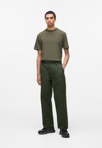 Camiseta de manga corta verde oliva combinada con pantalones holgados de un verde oscuro y zapatillas negras, con un diseño simple y forma recta.