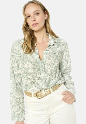 Camicia a maniche lunghe in crema chiaro con stampa floreale verde; presenta un colletto con bottoni ed è abbinata a pantaloni bianchi a vita alta e una cintura intrecciata.
