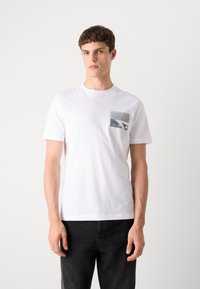 Hvid bomulds T-shirt med korte ærmer og en brystlomme, der har et gråt fotografisk print. Klassisk rund halsudskæring og regular fit.