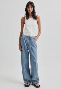 Könnyű, fehér ujjatlan felső, laza, világoskék csíkos nadrággal, ami rugalmas zsinórral állítható derékkal és oldalzsebekkel rendelkezik. Lapossarkú fekete szandál.