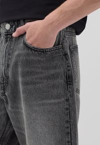 Jeans de denim gris con una textura ligeramente deslavada, diseño de cinco bolsillos, costuras visibles y un cierre de botón metálico en la cintura.