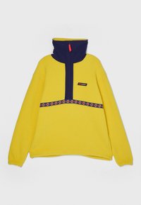 Fleece sweater in heldergeel met marineblauwe hoge kraag en halve rits. Heeft een decoratieve patroon band over het midden van het kledingstuk. Merkl logo zichtbaar.