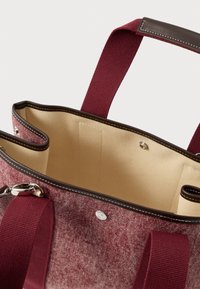 Τσάντα tote από βυσσινί ύφασμα με υφή, διακοσμημένη με καφέ δερμάτινες λεπτομέρειες και μπεζ εσωτερικό. Διαθέτει εσωτερικές τσέπες και μεταλλικά εξαρτήματα.