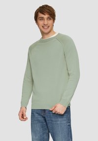 Hellgrüner Rundhalsausschnitt-Pullover mit langen Ärmeln, gerippten Bündchen und Saum, kombiniert mit blauen Denim-Jeans. Glatte Textur und lässige Passform.