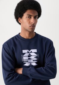 Sudadera azul marino hecha de una mezcla de algodón, con un gran diseño gráfico blanco en la parte frontal. Cuello y puños acanalados, corte relajado.