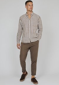 Gestreepte bruine en witte button-up shirt gecombineerd met bruine tapered broeken en donkere schoenen, met een kraaghals en opgerolde mouwen.